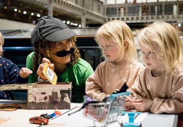 A researcher dressed up as a detective shows two young children an email symbol 